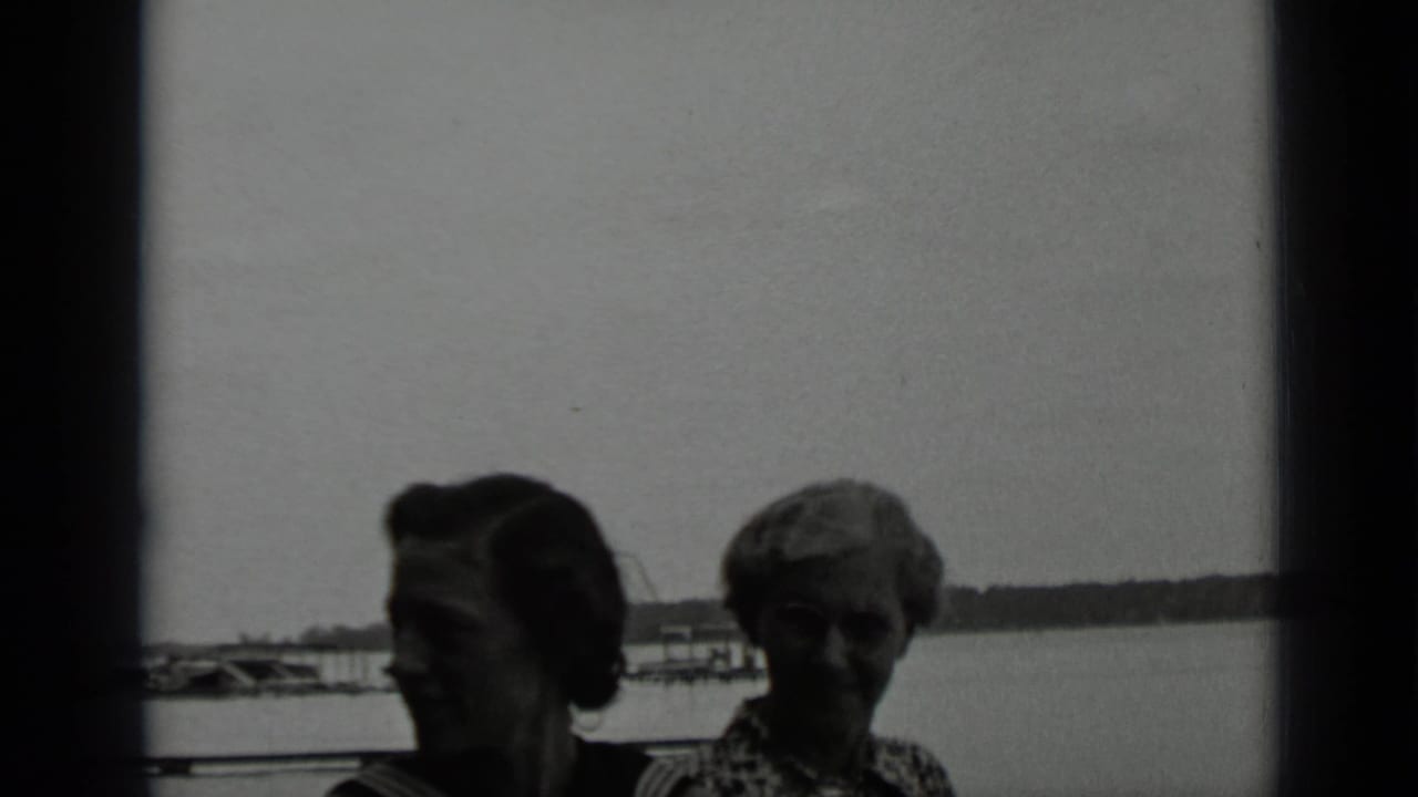 Two women stand by a lake with docks and shoreline behind them.