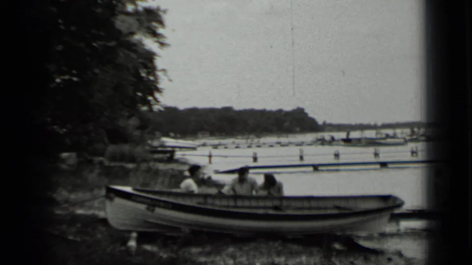 A small boat with people aboard sits near the Clear Lake shore, with trees, docks, and water visible in the background.