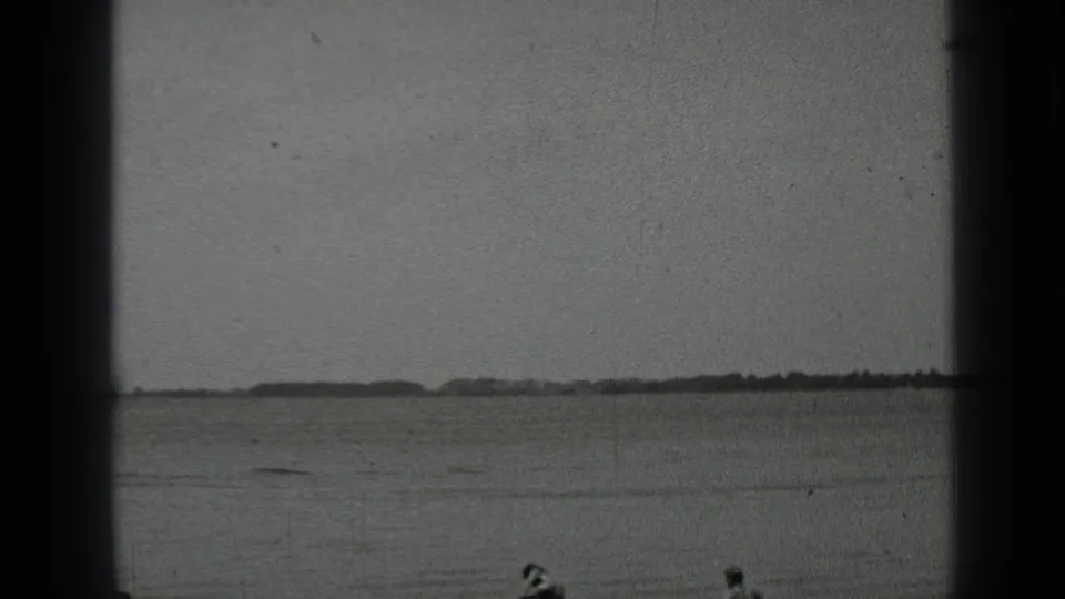 Clear Lake home-movie frame showing swimmers far from camera in open water, with a low shore on the horizon.