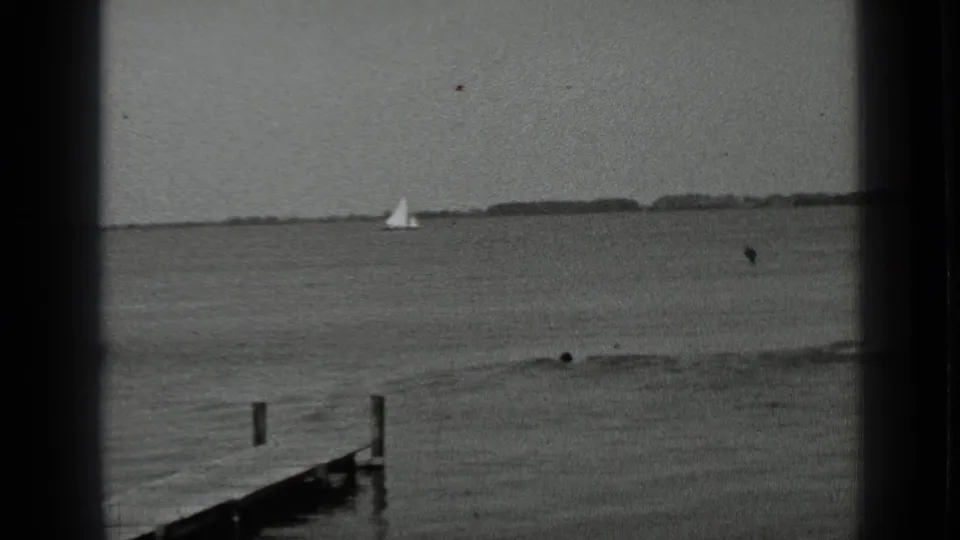 1939 Clear Lake frame with a small sailboat in the distance, swimmers near shore, and a wooden jetty at lower left.