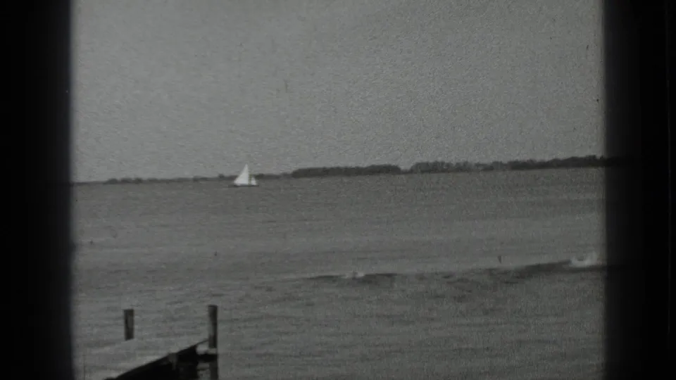 Clear Lake, California home-movie still showing a distant sailboat, foreground jetty posts, and calm lake water in 1939.