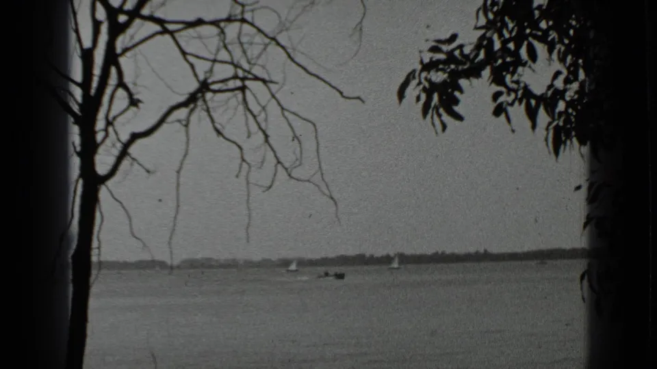 Clear Lake appears through tree branches and leaves, with small boats moving or resting far out on the water in the 1939 home-movie frame.