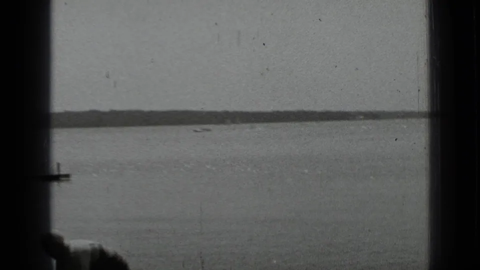 Black-and-white lakeside view at Clear Lake with a small boat on the water, a distant shoreline, and part of a dock at the left edge.