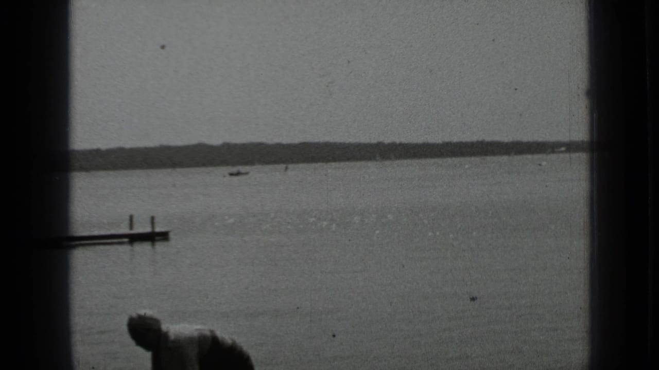 Calm lake with distant shoreline and part of a person at the lower edge.