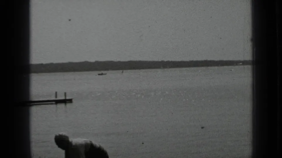 1939 Clear Lake, California home-movie frame showing calm water, distant shoreline, a dock edge, and a partial figure in the foreground.