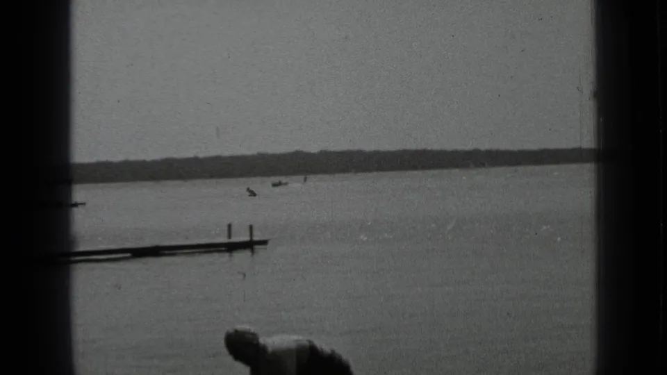 Clear Lake home-movie frame with a small dock, distant boats, shoreline, and a partial person at the bottom of the frame.