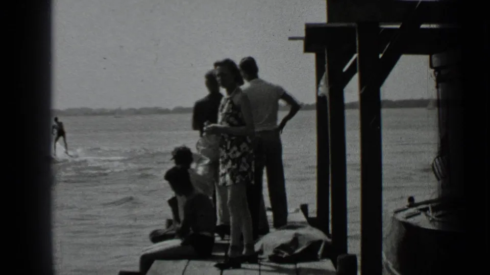 1939 Clear Lake, California frame showing adults in period casual clothing gathered on a wooden dock beside the water.