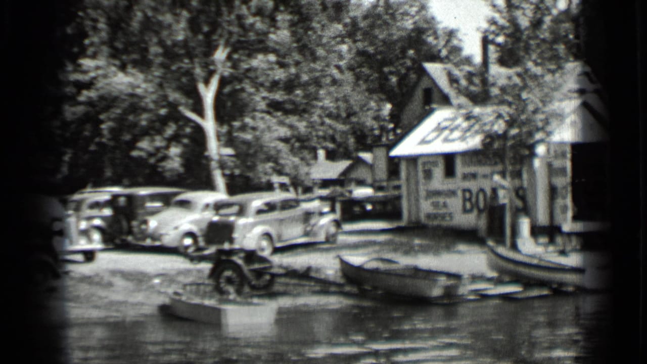 Clear Lake, California home-movie frame from 1939 showing a boathouse with a BOATS sign, parked late-1930s cars, boats, trees, and shoreline water.