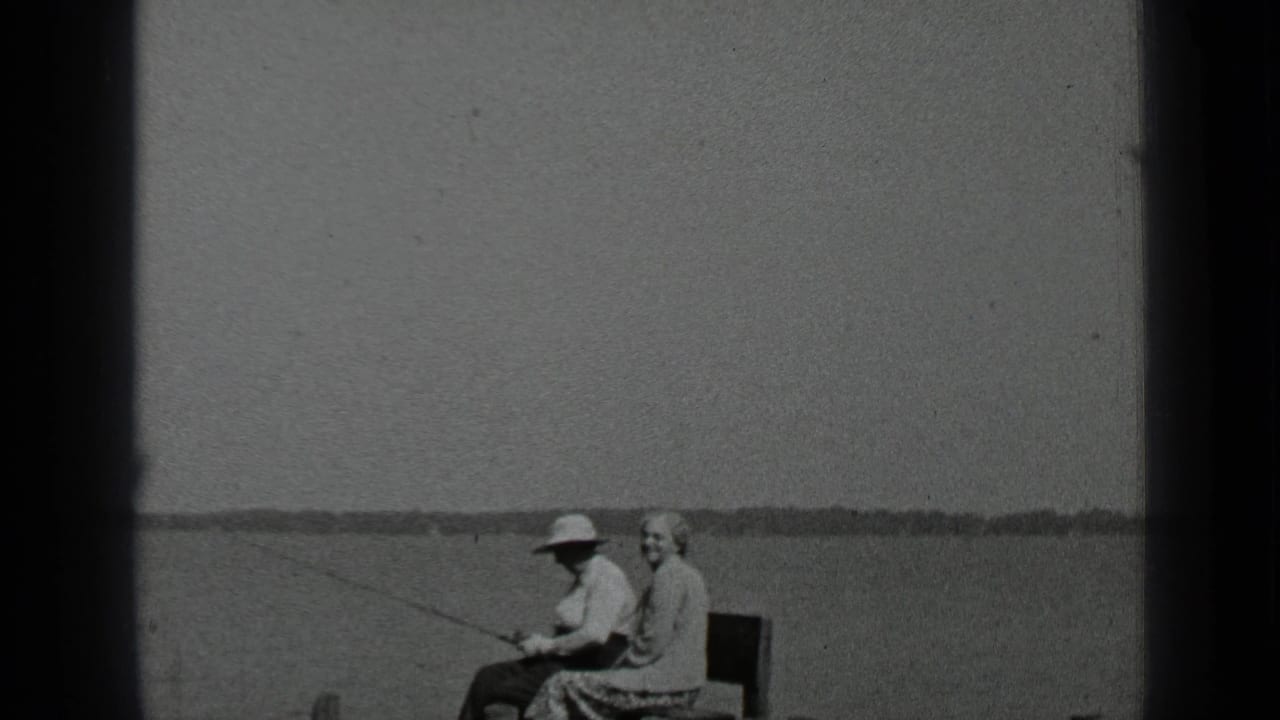 Couple seated on a bench by a lake, with the man holding a fishing rod.