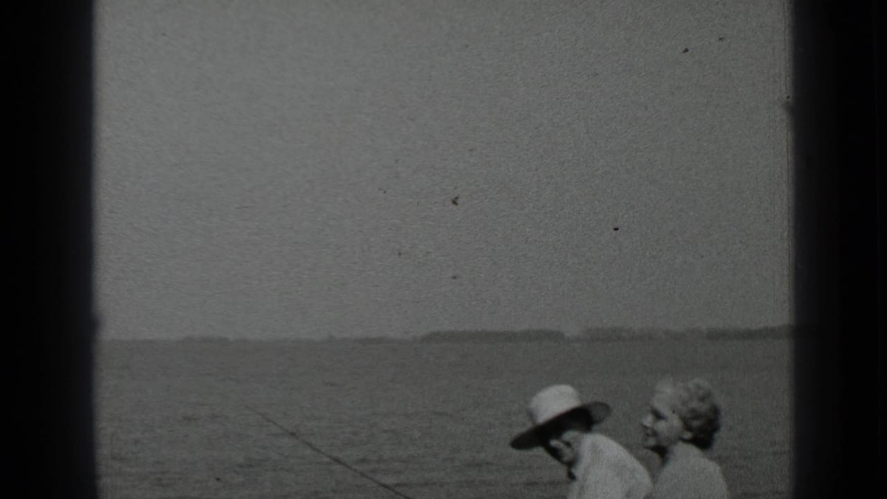 Two seated adults by the lake, with a fishing rod extending over the water.