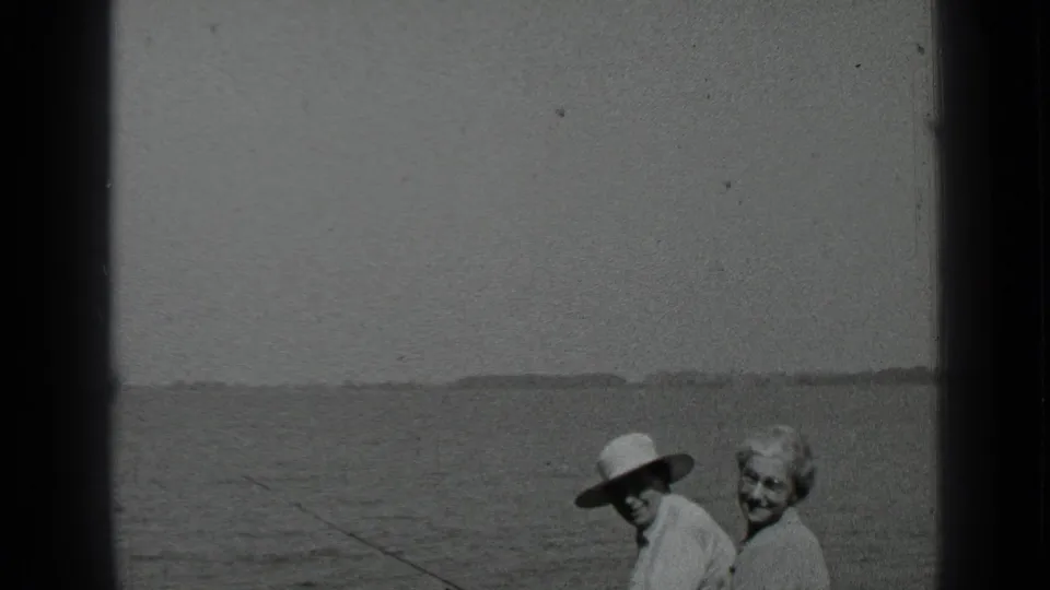 Final 1939 Clear Lake frame showing the couple smiling on the bench, with the fishing rod crossing the water in the foreground.