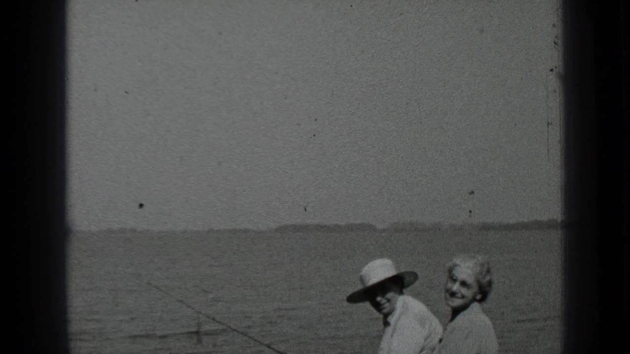 Older couple smiling near a lake, with the man in a wide-brimmed hat.