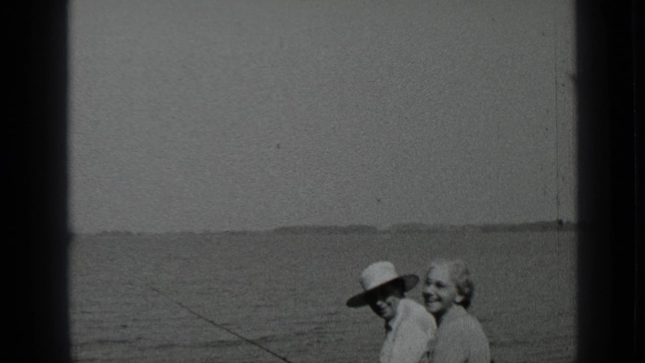 Older couple beside calm water, with a faint shoreline in the distance.