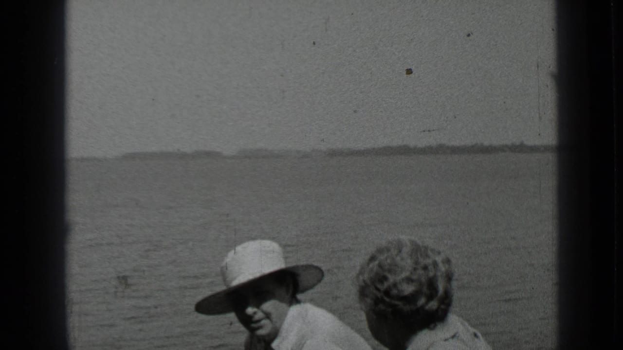 Two adults seated on a boat with lake water and a distant shoreline behind them.
