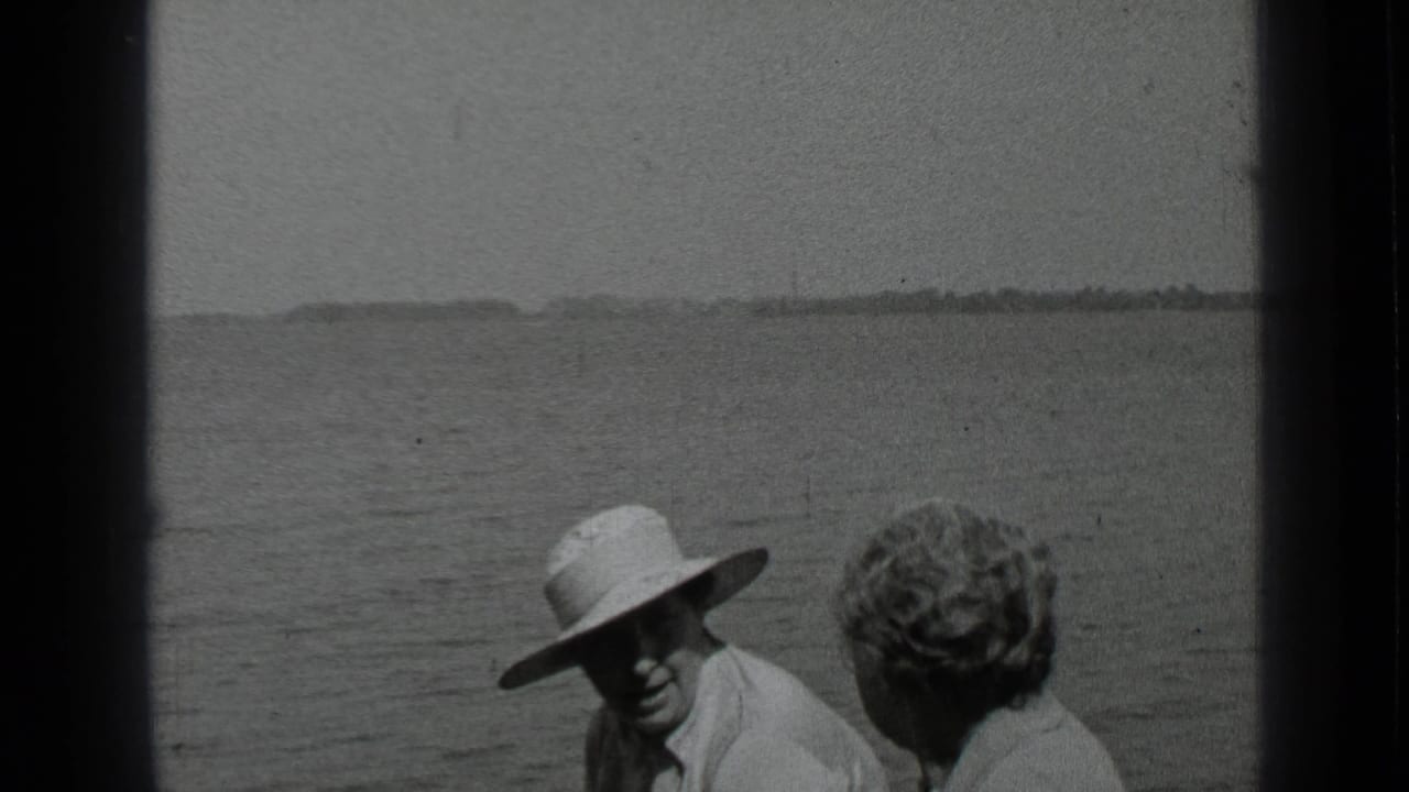 Adult in a white hat faces the camera while another adult sits beside them on a boat.
