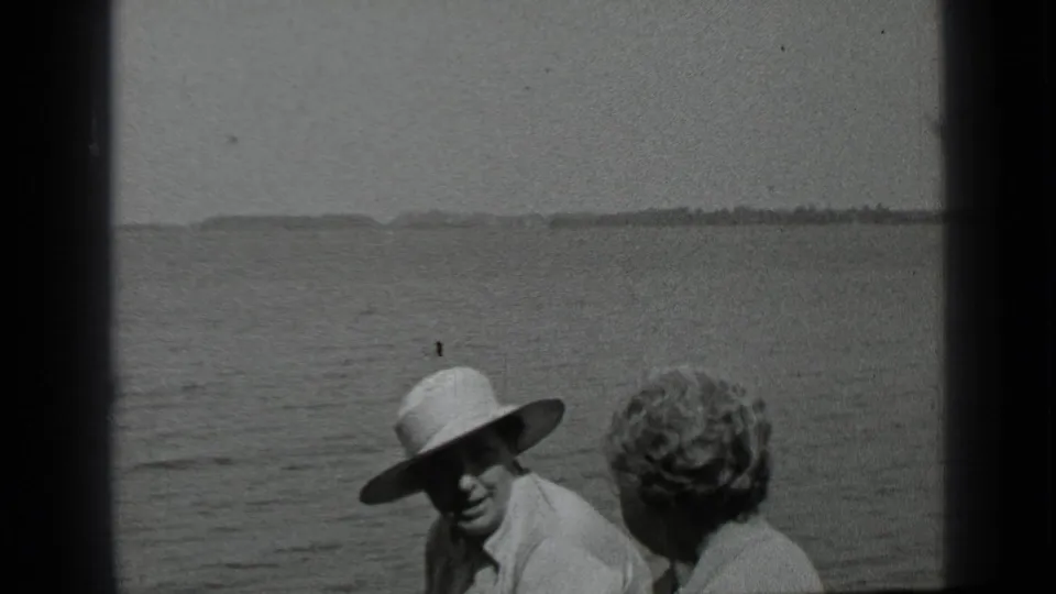 1939 Clear Lake frame with two adults seated close together on a boat, the hat brim shading one face as water stretches behind them.