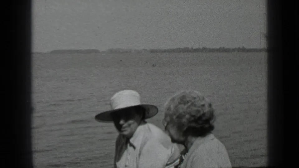 A 1939 Clear Lake home-movie still shows two adults on a boat, with one smiling under a white brimmed hat beside the water.