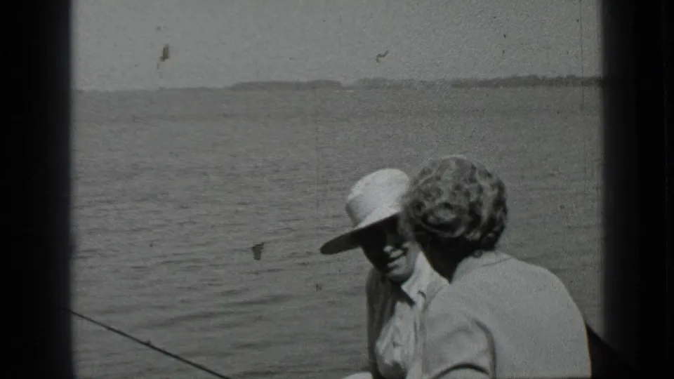 The woman faces the man in the wide-brimmed hat on a boat at Clear Lake, with open water and a low shoreline beyond.