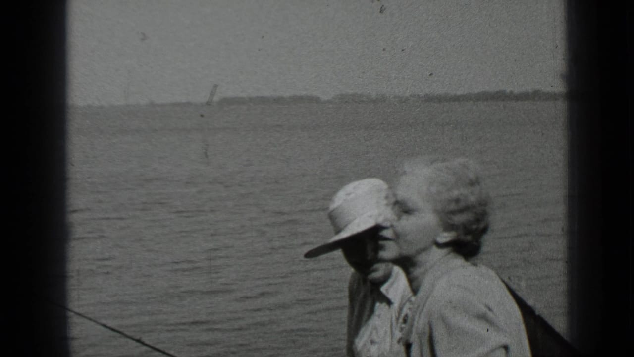 Two adults sit in a boat on a lake, with one wearing a light brimmed hat.