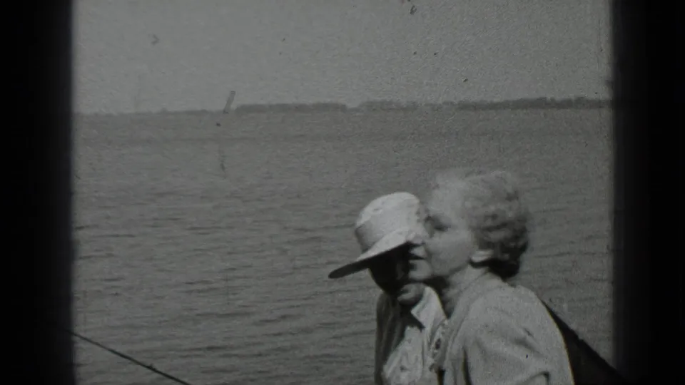 1939 Clear Lake home-movie frame showing two adults seated in a boat, water and distant shoreline behind them.