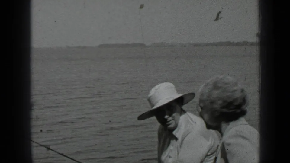 Black-and-white 8mm frame from Clear Lake showing a hat-wearing man and a woman seated in a boat near open water.