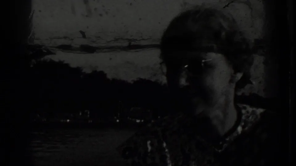 Underexposed Clear Lake home-movie frame with a person close to the camera and the lakeshore visible in the background.