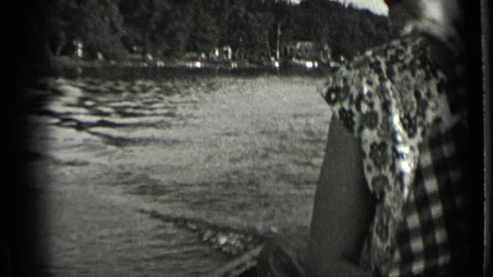 Clear Lake boat-view frame with a passenger partly visible at right, rippled water, and tree-covered shoreline in the distance.