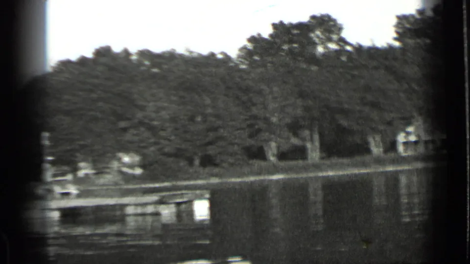 1939 Clear Lake view with calm water, dense trees, a low dock, and small buildings along the opposite shore.