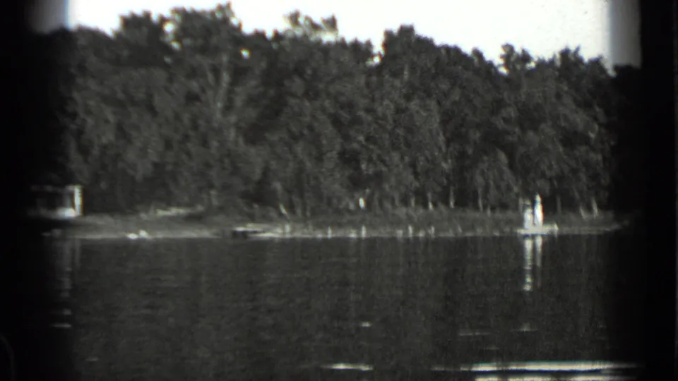 Clear Lake shoreline in 1939, with dense trees, smooth water, and a small bright shoreline object or craft at right.