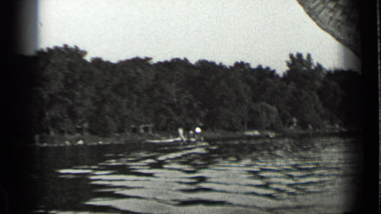 Clear Lake shoreline in 1939 with textured water, a small boat near shore, and distant people against trees.