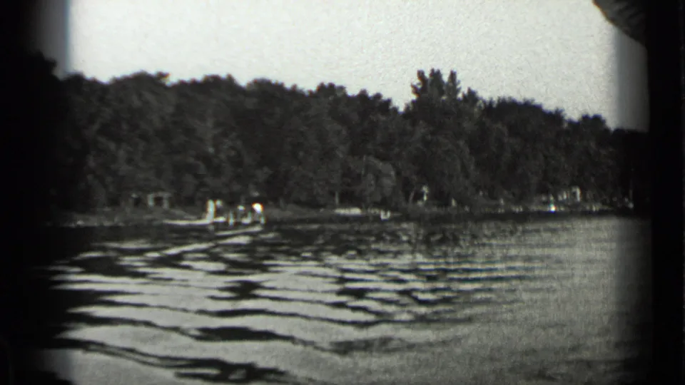 1939 Clear Lake view with low ripples in the foreground and small distant figures along a wooded lakeshore landing.