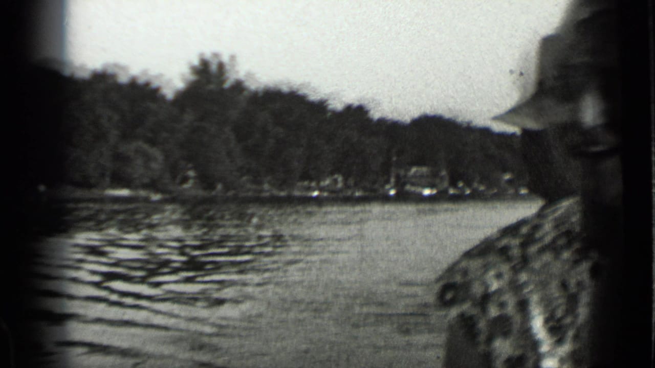 1939 Clear Lake home-movie frame with a man partly cut off at the edge, rippled water, trees, and distant boats.
