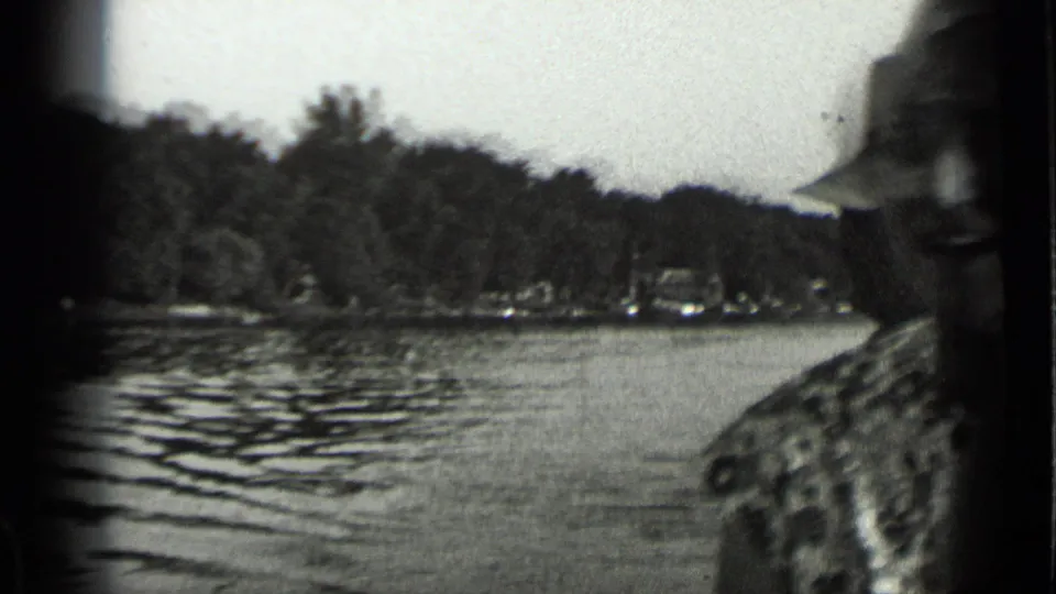 1939 Clear Lake home-movie frame with a man partly cut off at the edge, rippled water, trees, and distant boats.