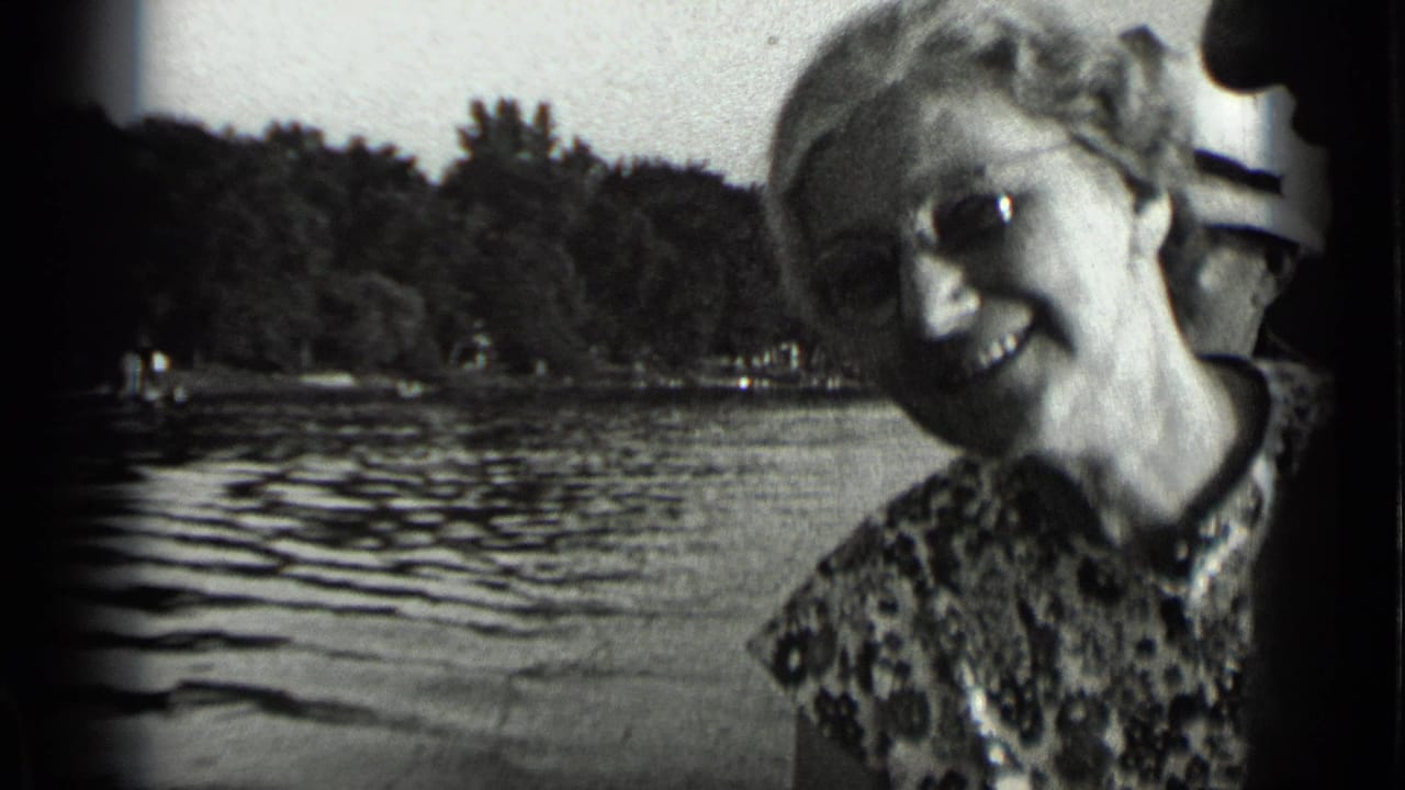 Smiling woman in glasses near Clear Lake, California, with rippled water and a wooded shoreline behind her.
