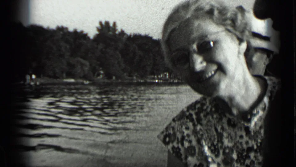 Smiling woman in glasses near Clear Lake, California, with rippled water and a wooded shoreline behind her.