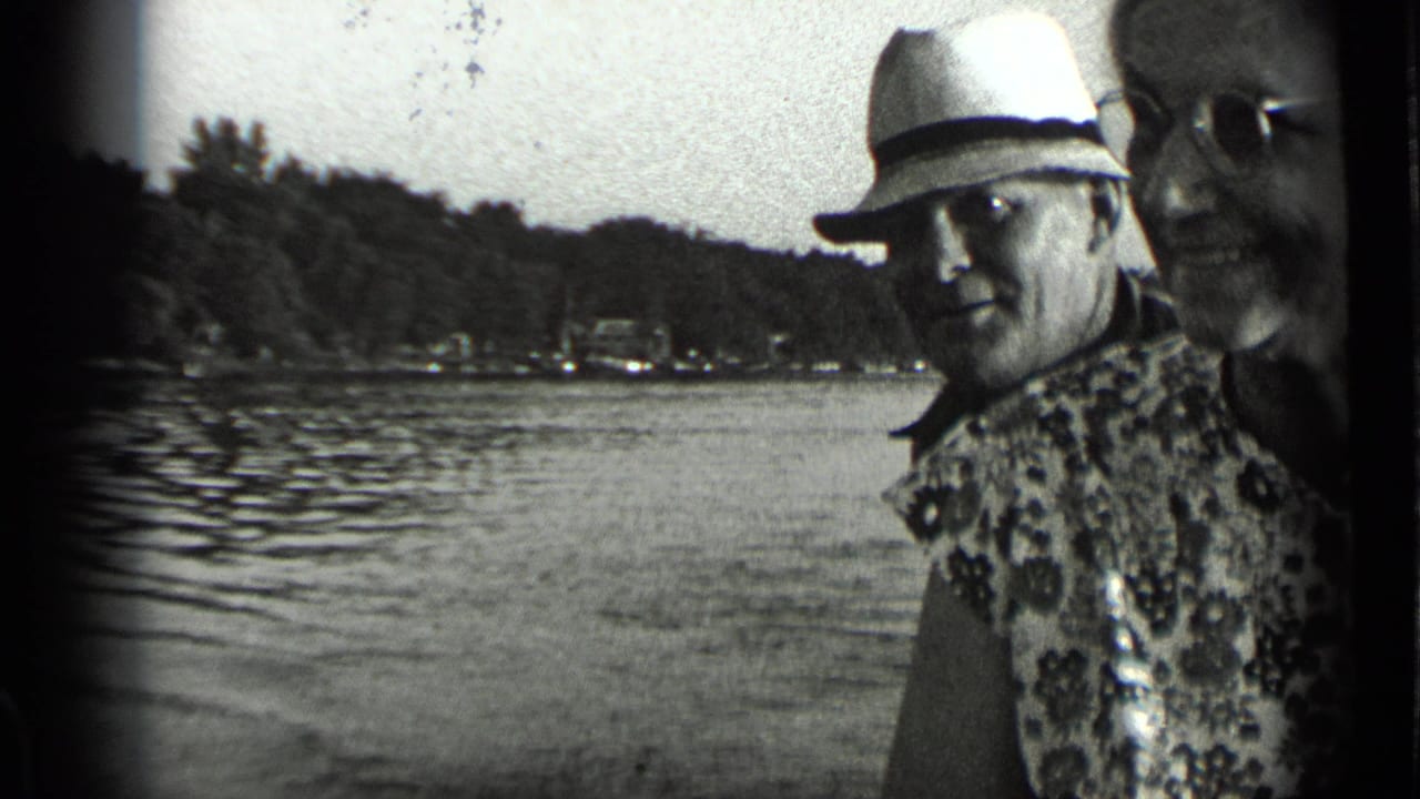 At Clear Lake, California, in 1939, a man in a light fedora and patterned shirt stands beside a woman in glasses near rippled water.