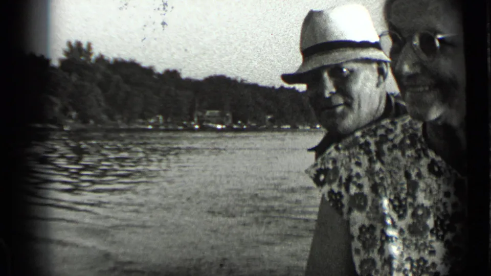 At Clear Lake, California, in 1939, a man in a light fedora and patterned shirt stands beside a woman in glasses near rippled water.