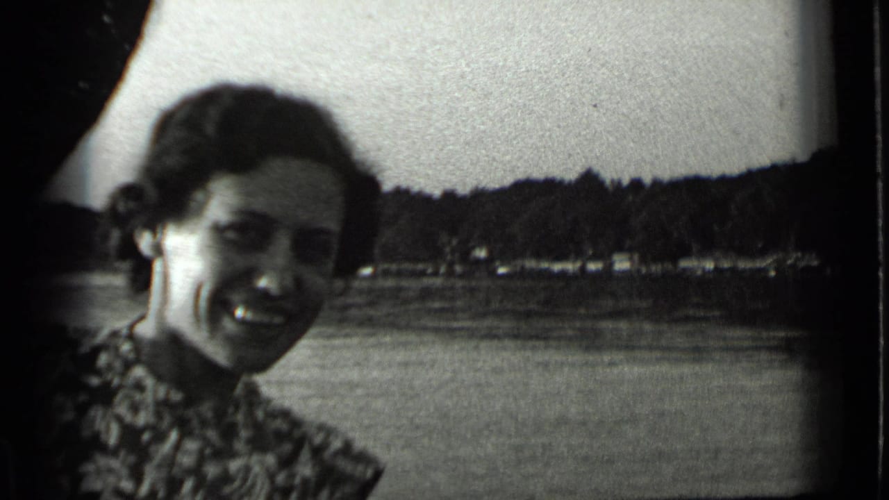 A smiling woman in patterned clothing faces the camera beside Clear Lake, California, with water and a wooded shoreline behind her.