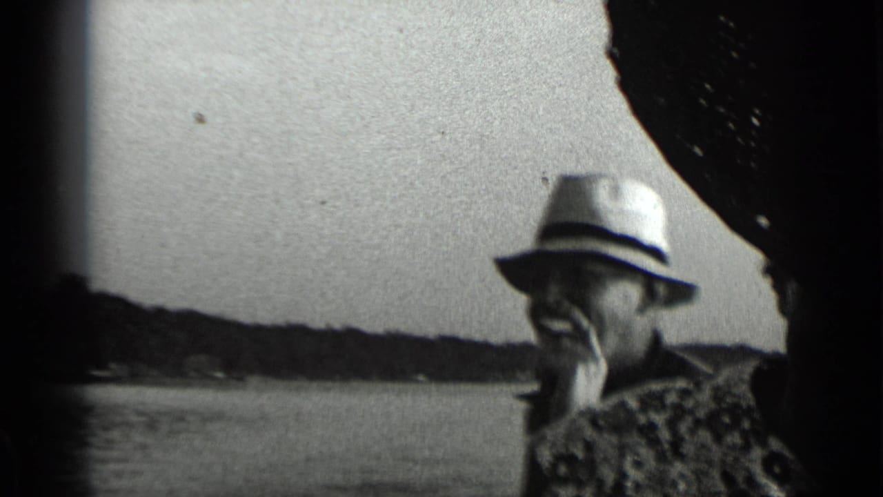 1939 Clear Lake frame of an older man in a light hat smoking on a moving boat, with water and wooded shoreline in the background.