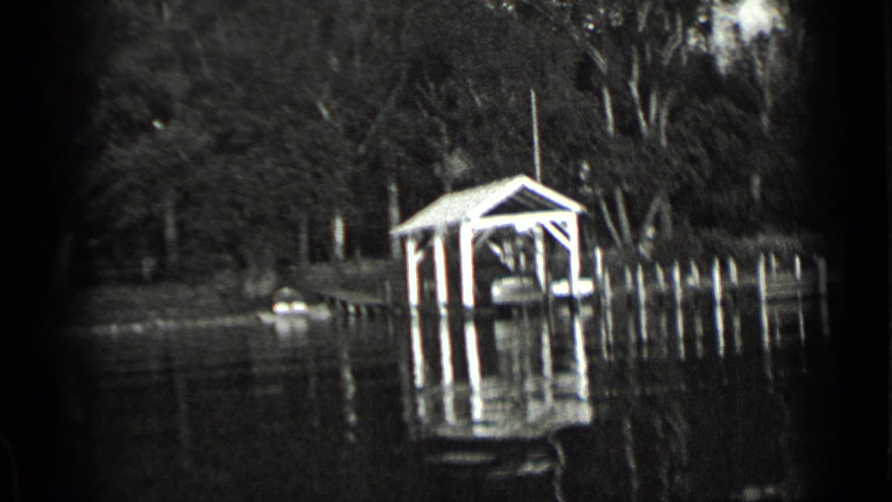 1939 Clear Lake home-movie frame showing a covered boathouse, dock pilings, shoreline trees, and water reflections.