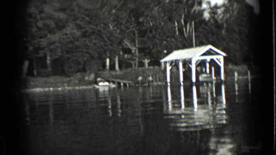 1939 home-movie still of a lakeside boathouse or covered dock at Clear Lake, framed by trees and reflective water.