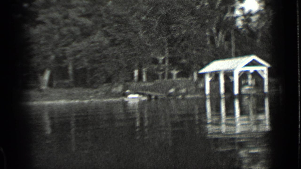 1939 Clear Lake home-movie frame showing high water around a covered shoreline shelter, dock posts, trees, and water reflections.