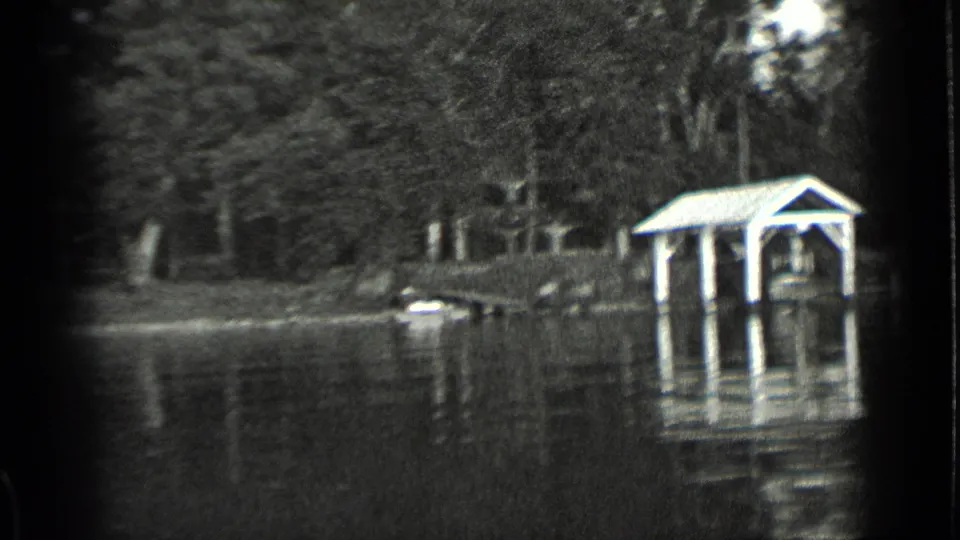 1939 Clear Lake home-movie frame showing high water around a covered shoreline shelter, dock posts, trees, and water reflections.