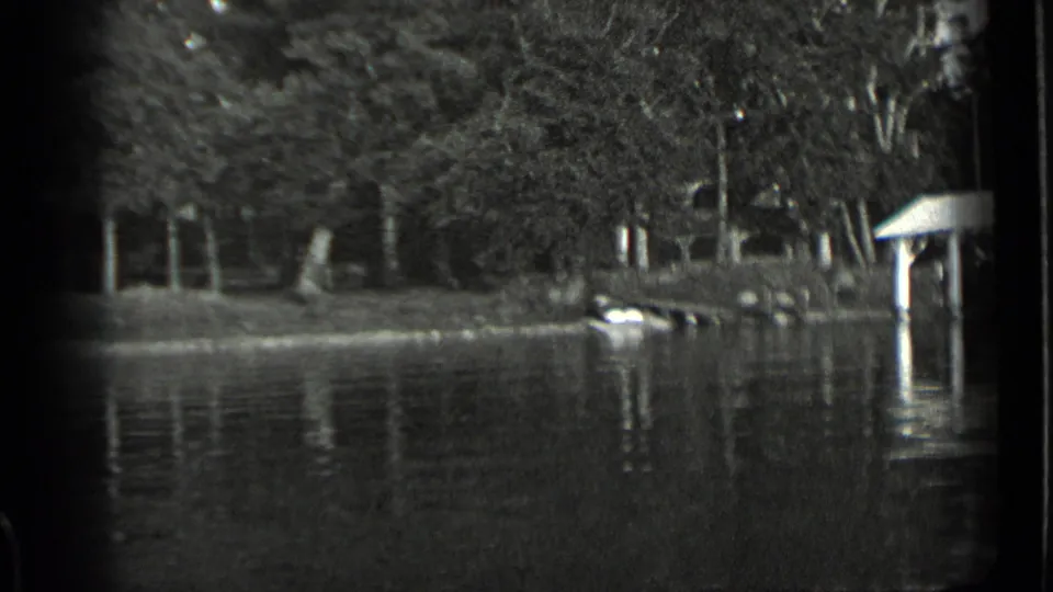 Clear Lake shoreline view with calm high water, trees, submerged dock elements, and a covered structure partly visible at the frame edge.