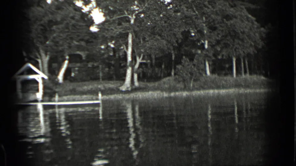 1939 Clear Lake flood scene with a small covered shelter, submerged dock posts, calm reflective water, and a wooded bank.