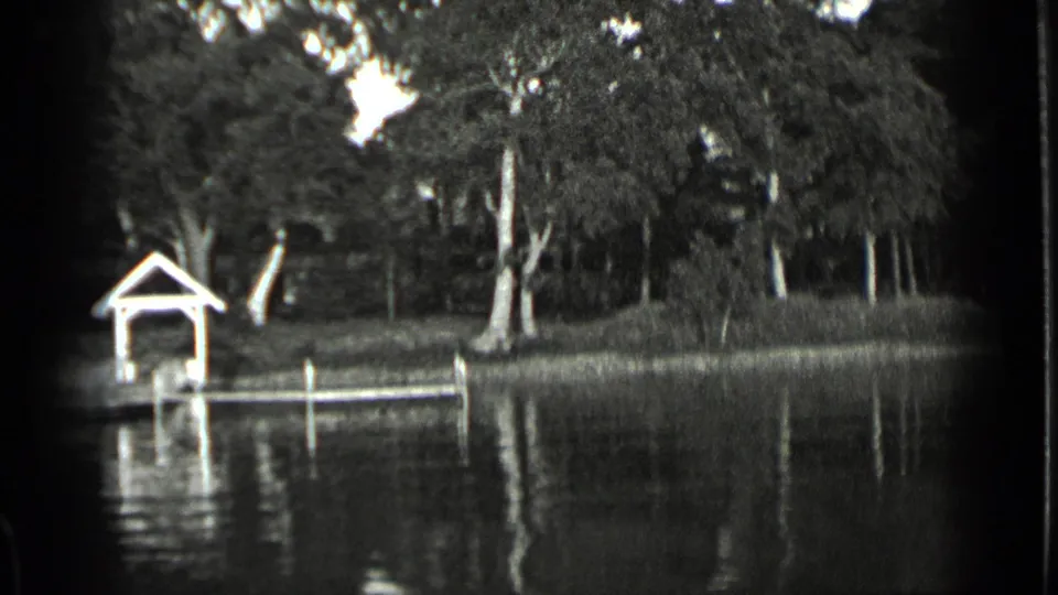 1939 Clear Lake, California home-movie frame showing a covered wooden dock, shoreline trees, posts, and reflections on still water.