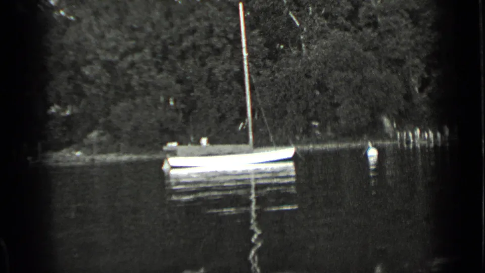 1939 Clear Lake home-movie frame showing a small sailboat on calm water near a wooded shore and a floating marker.
