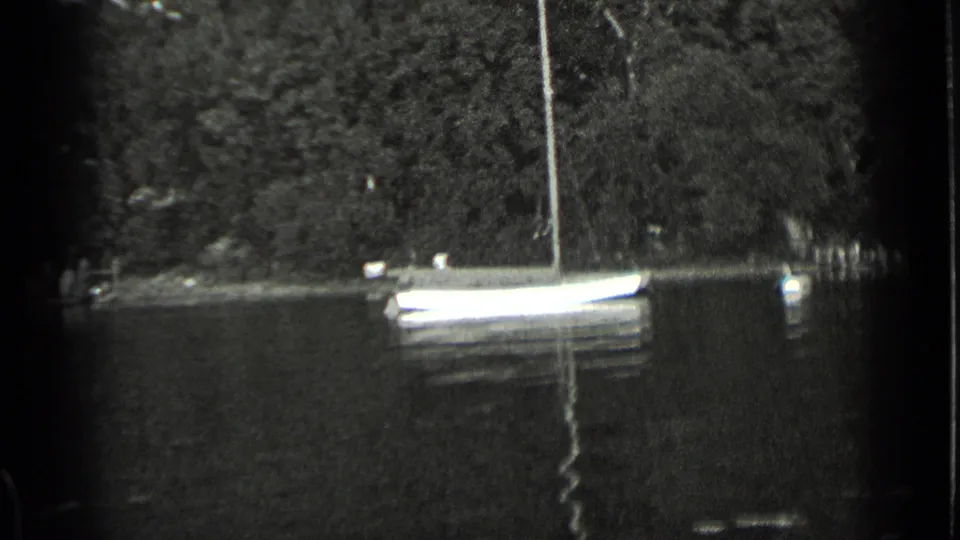 1939 Clear Lake home-movie frame showing a small sailboat near the wooded shoreline with its reflection on the water.
