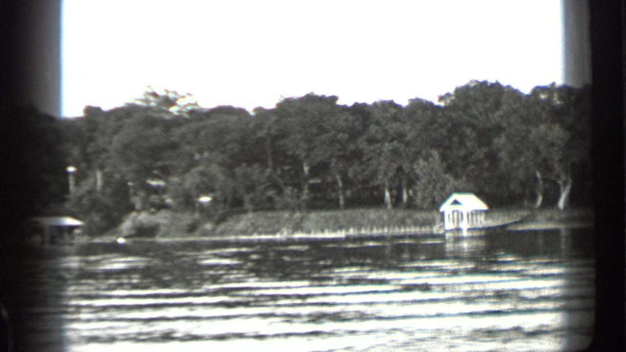 Clear Lake shoreline seen from the water, with dense trees and a small white boathouse or dock shelter near the bank.