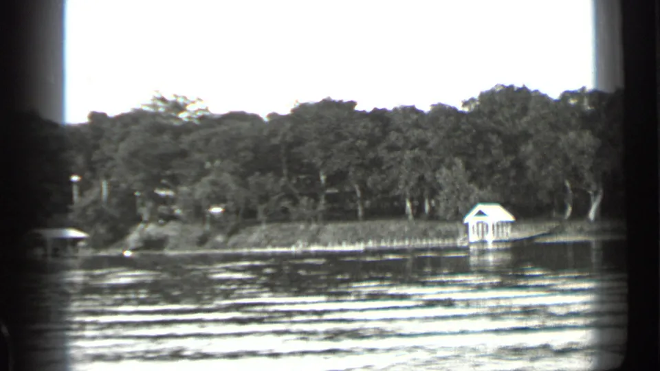 Clear Lake shoreline seen from the water, with dense trees and a small white boathouse or dock shelter near the bank.